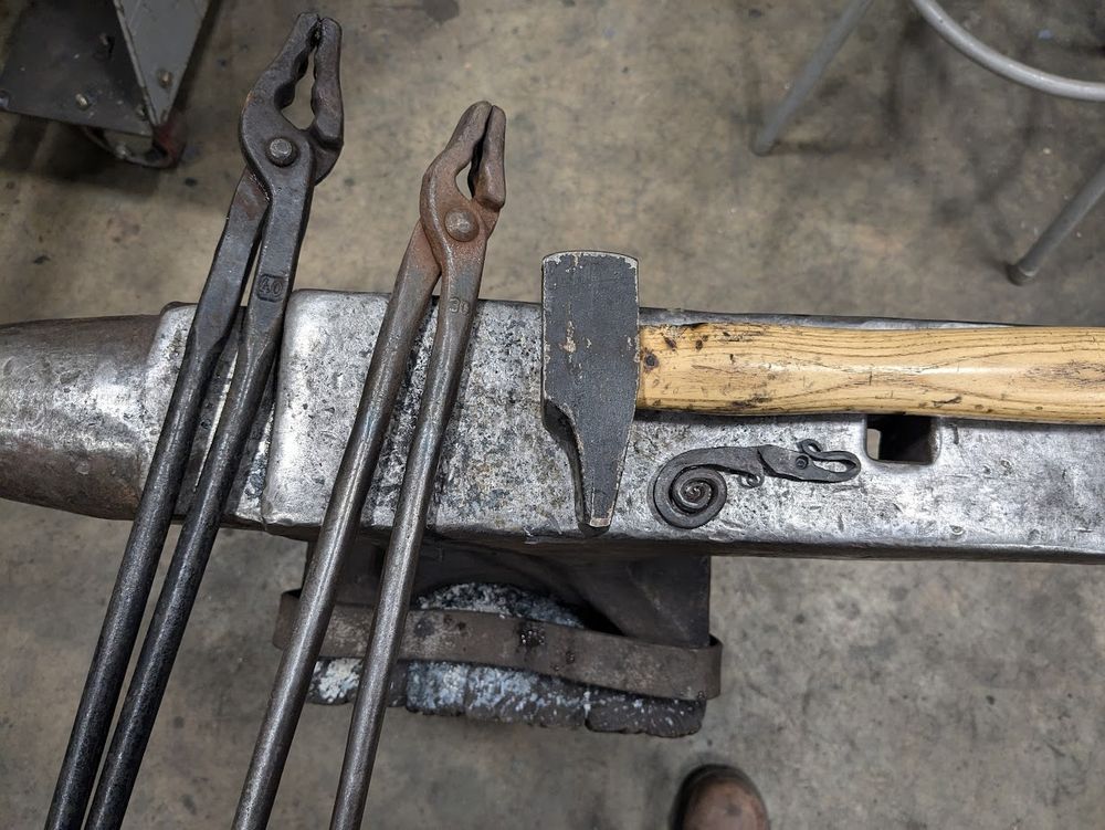 A small dragon pendant on an anvil with tongs and a hammer
