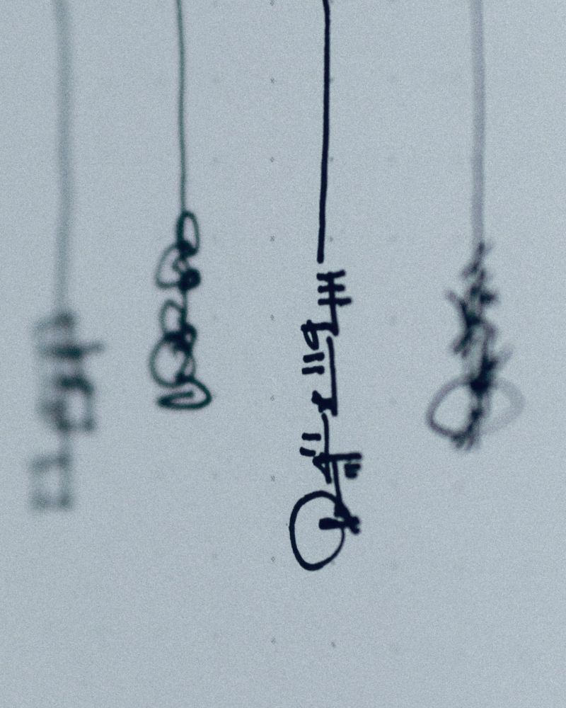 Freehand asemic figures are drawn such that they appear to hang suspended from cords at various distances from the camera lens