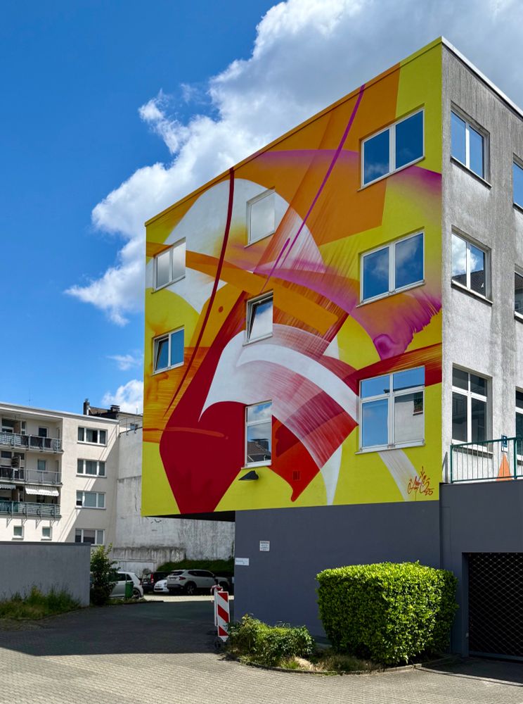 A mostly yellow, orange, red mural by street artist MadC in the city center of Wuppertal.