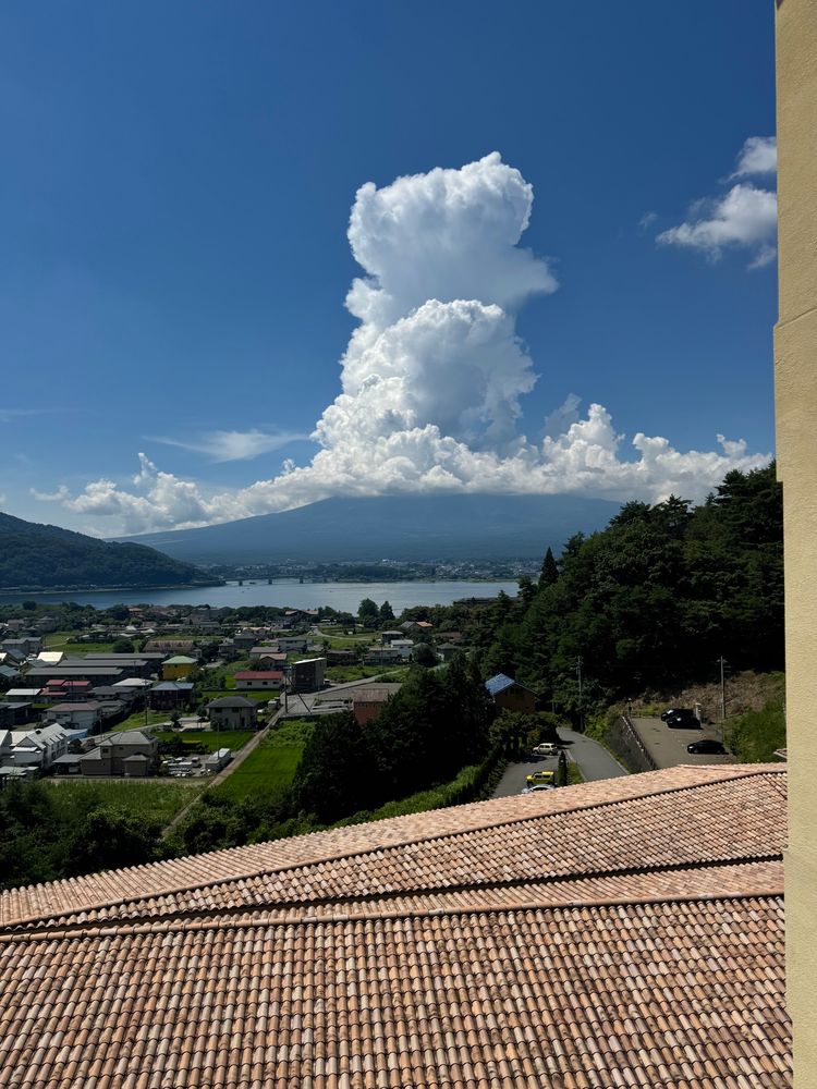 Mt. Fuji viewed on the horizon with a large vertical stack of clouds covering the top looking ominously like a plume of volcanic smoke. 
