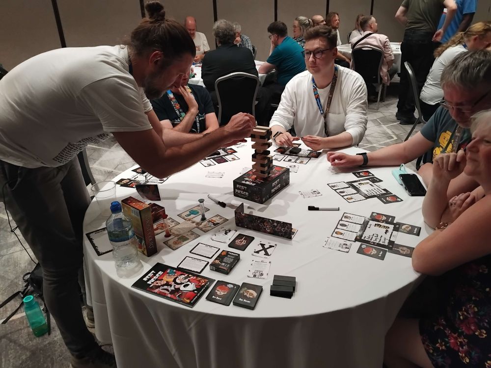 A player leans over to draw a block from the Jenga tower in a game of "Rest in Pieces"