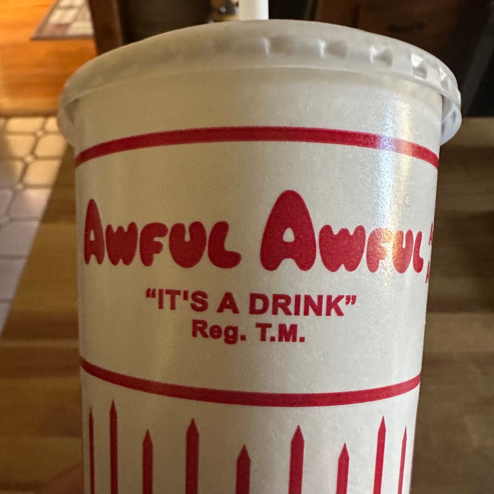 An Awful Awful drink cup. It’s a milk shake from Newport Creamery for those not in the know. 
The cup is white with red lettering. It reads:
“Awful Awful”
“It’s a Drink”™️