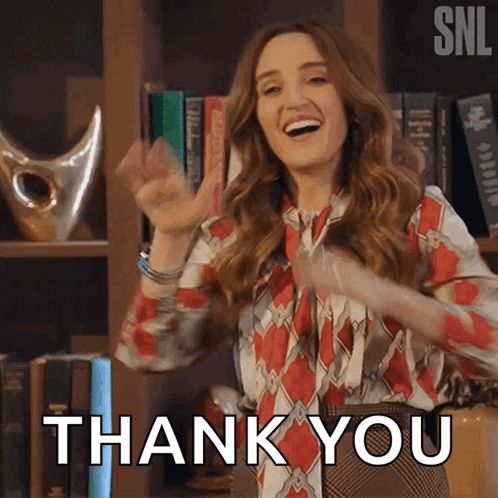 a woman is standing in front of a bookshelf and giving a thank you sign