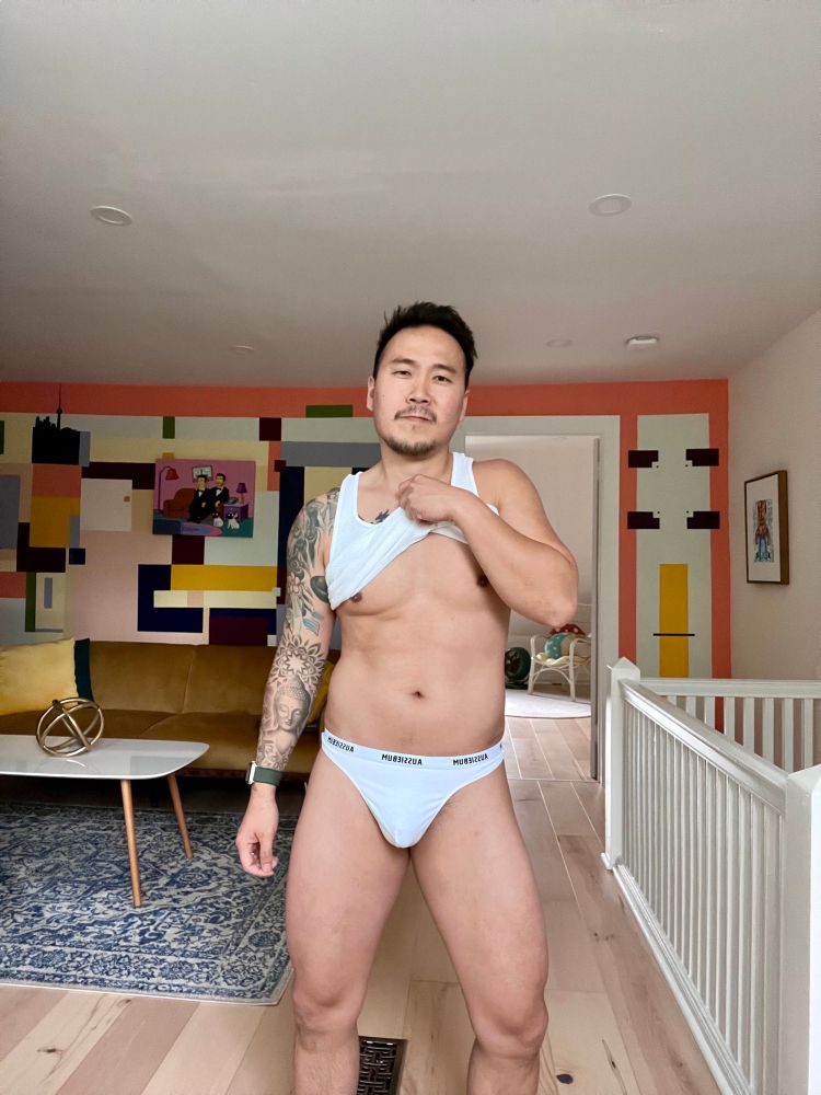 Man posing in white briefs and tank top lifted up to show midsection 