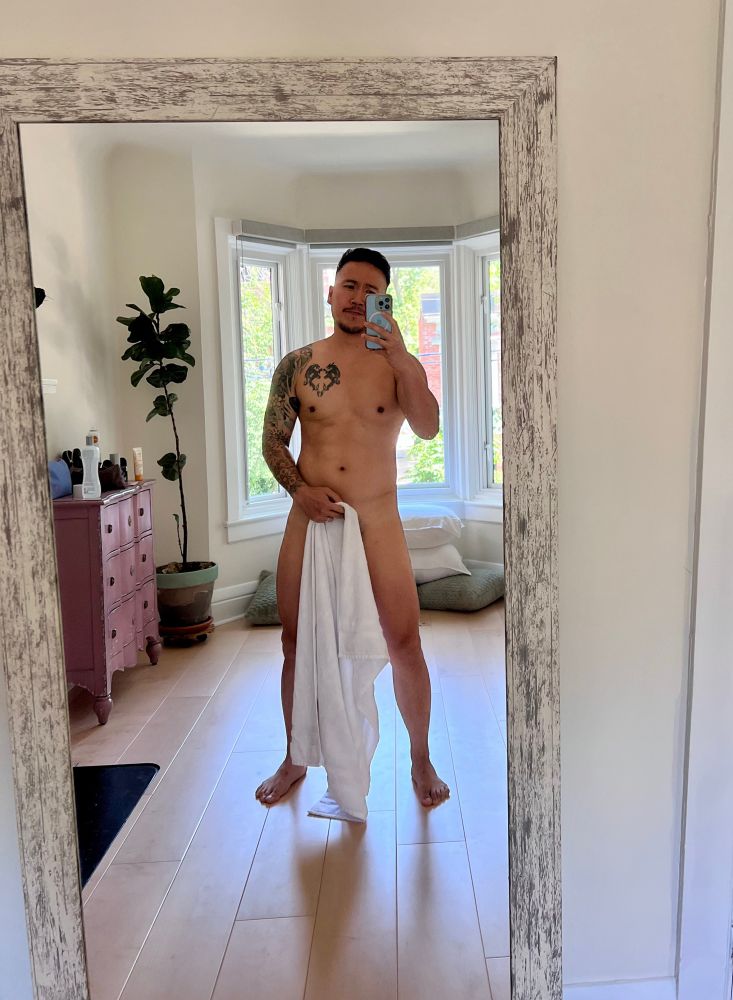 Naked mirror selfie of man holding towel to hide crotch area