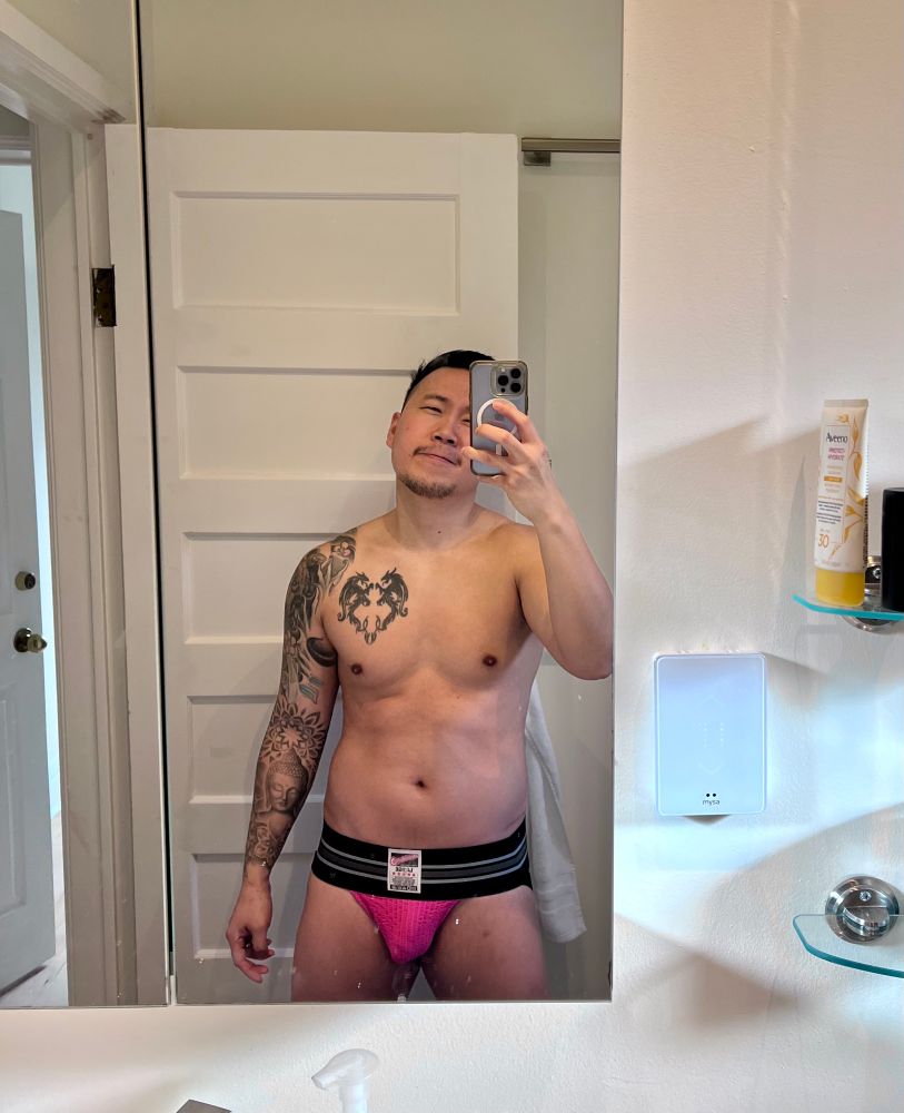Mirror selfie of man wearing a black and pink jockstrap showing vpl