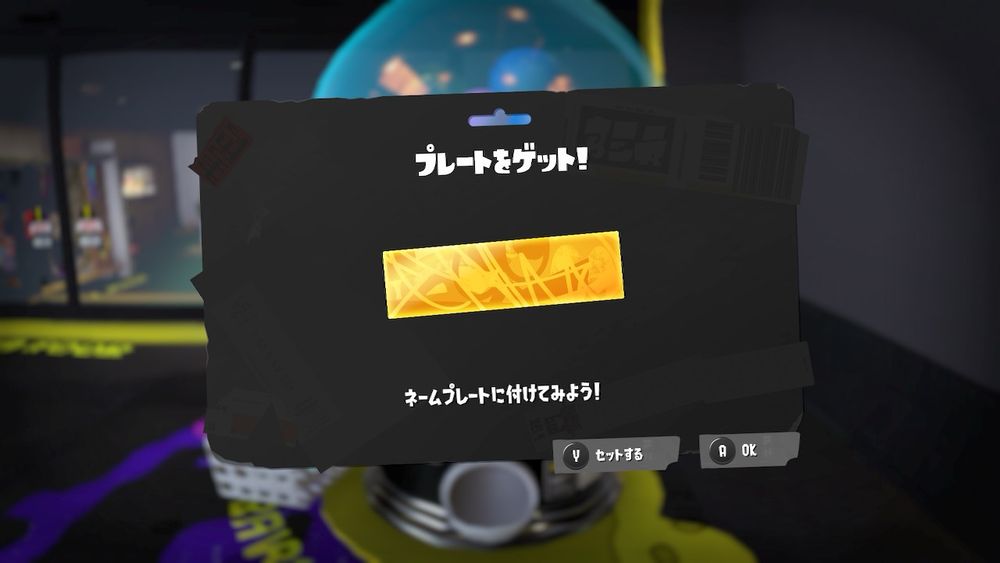 スプラトゥーン3ゲーム画面。ロビーのガシャポンくじで当たった金のプレート。