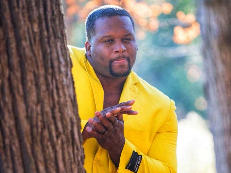 Popular meme pic of a Black man in a yellow suit leaning from behind a tree doing some sort of scheming hand rubbing gesture. Like Montgomery Burns but sexy.