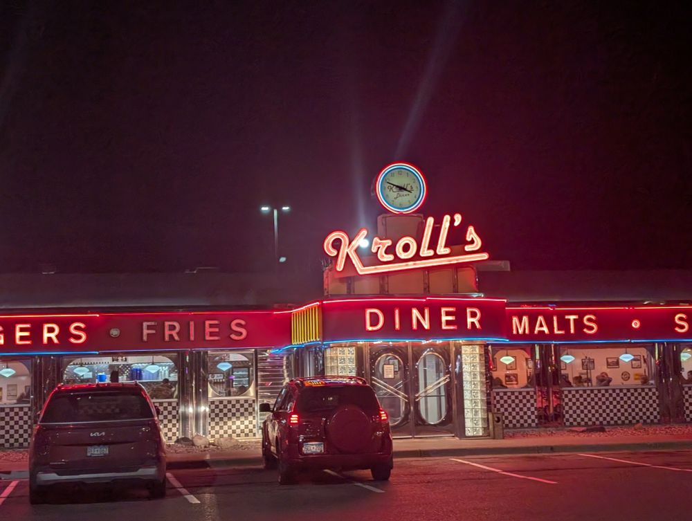 Nighttime photo of an old school diner in Fargo, North Dakota, called Kroll's Diner. The diner is lit up with red neon signage.