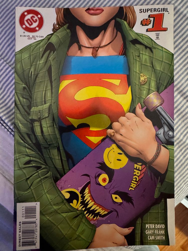 The cover of Supergirl #1 from 1996 by Peter David, Gary Frank and Cam Smith. The cover shows a mid-close up of Supergirl from her nose to her waist wearing a VERY 90s flannel and woven bracelet over her traditional Supergirl costume and carrying a skateboard. 