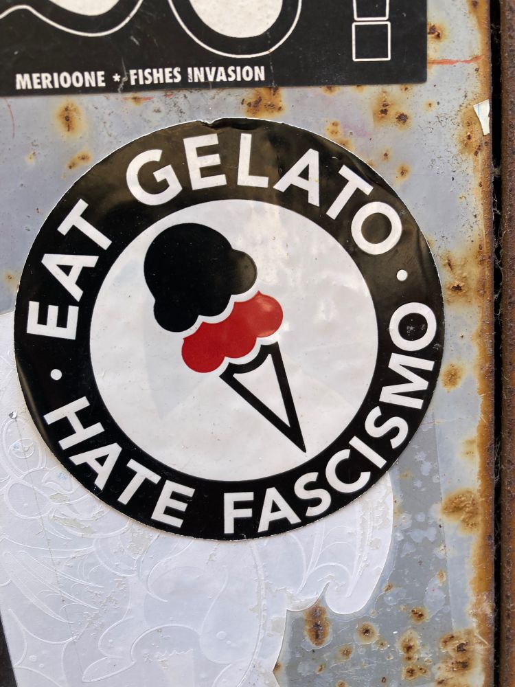 Black thick circle with the cartoon of an ice team inside. On the black circle:” eat gelato, hate fascismo”.