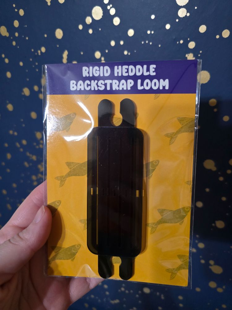 A rigid heddle backstrap loom packaged to sale and attached to a card.
