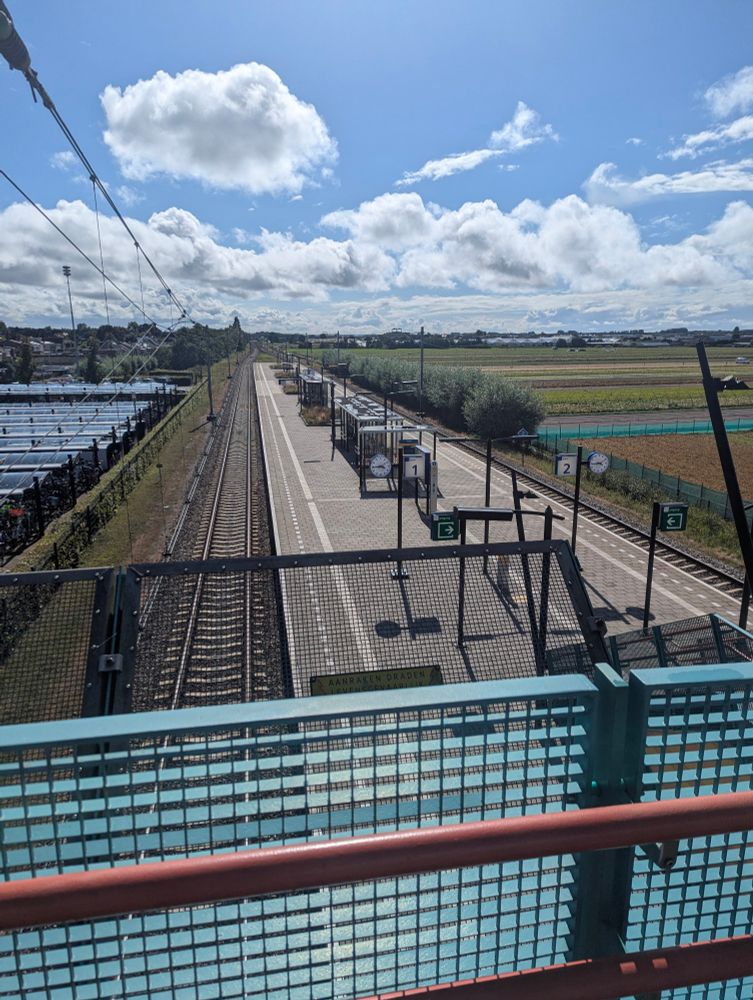Hillegom railway station. An island platform, two tracks, horticultural nursery fields beyond. 