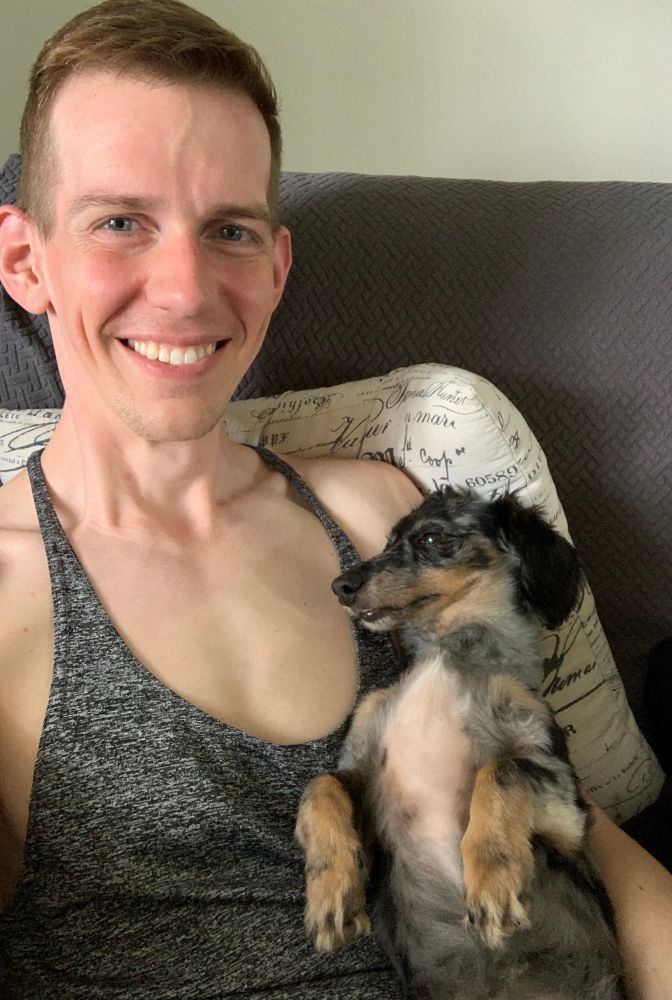 The sweetest miniature dachshund lying in the crook of her favorite smiling gay’s arm while on the couch