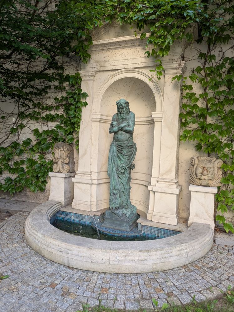 A bronze fountain, heavily oxidized,  in a beautiful carved alcove. 