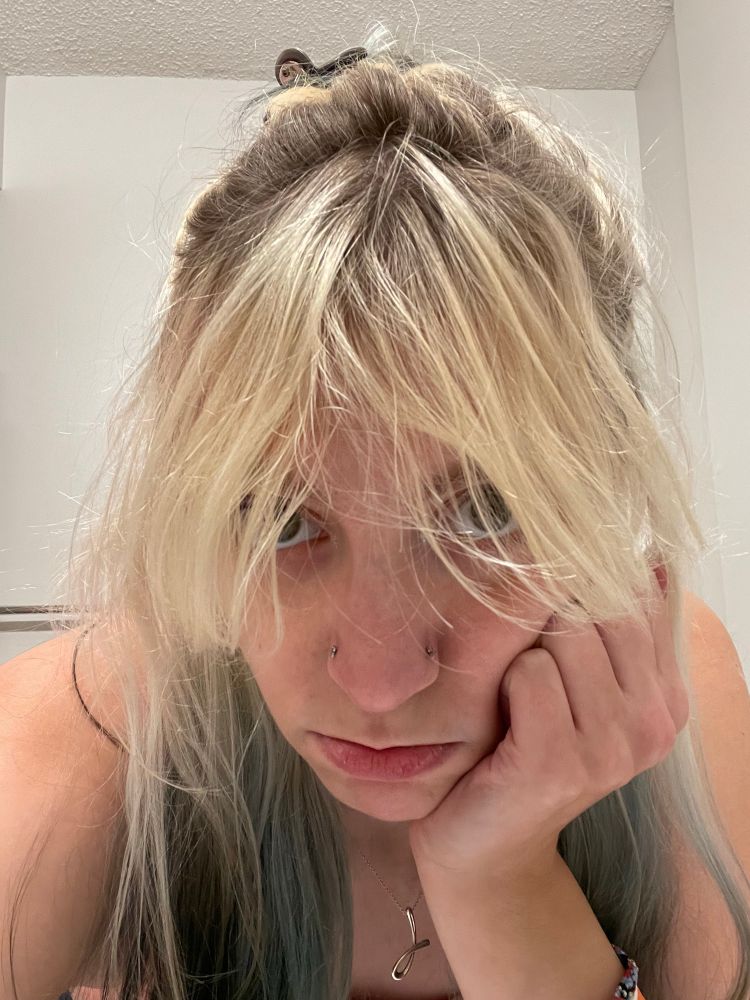 selfie of me with my bleach blonde bangs hanging down practically to the tip of my nose and my shitty terrible roots plainly visible. i'm leaning my chin and cheek in my fist and making a puppy pout of sorts. it's a rough photo tbqh