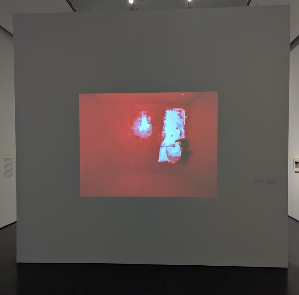 Man in white painter suit in a room he is painting red. Still shot from John Baldessari's video painting project 'Six Colorful Inside Jobs', 1977. On display at MCA Chicago.