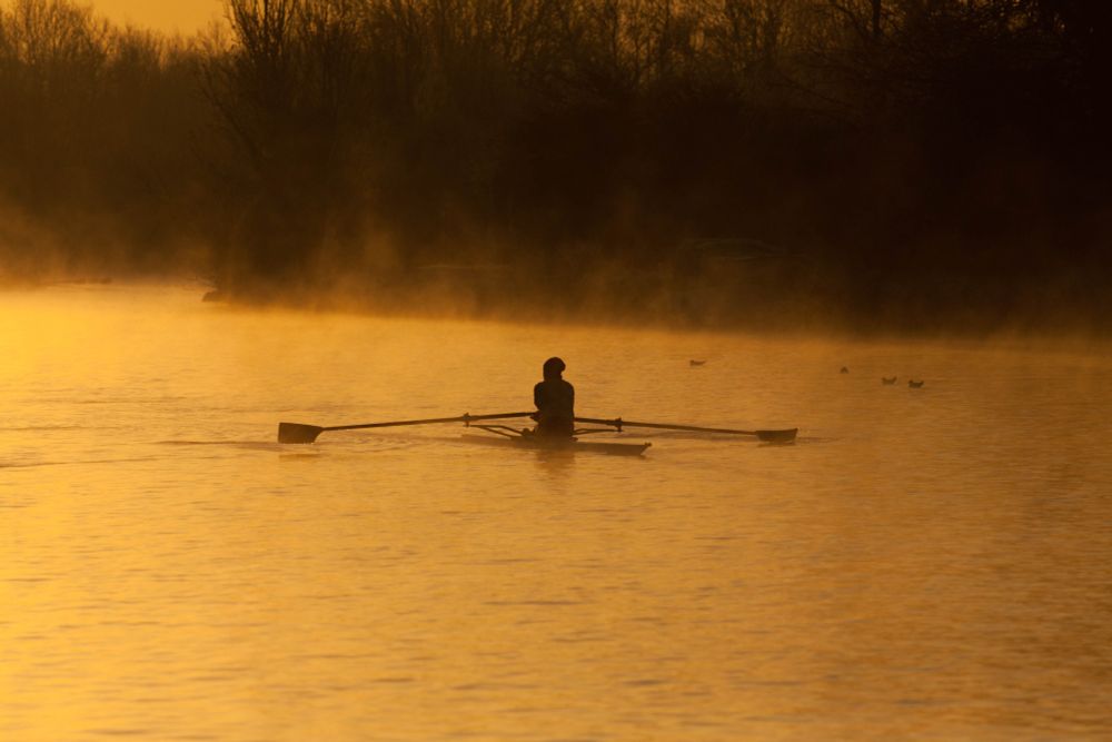 Single rower coming through mist on the river Thames at sunrise. 