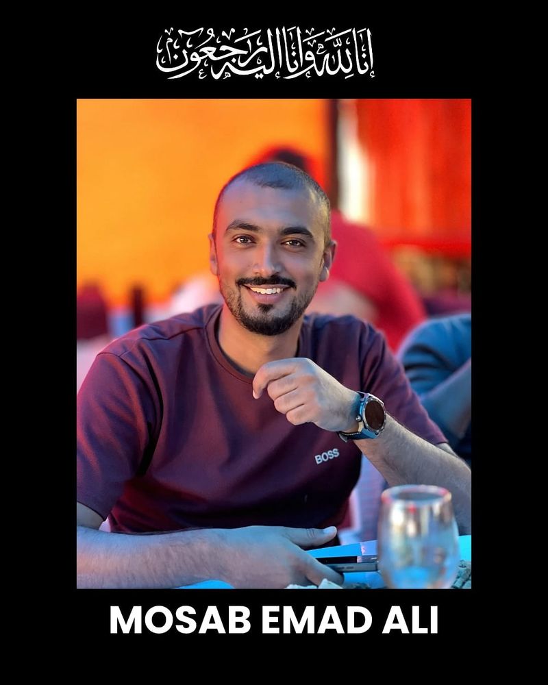 A sitting Mosab Emad Ali poses casually and smiles for a portrait.