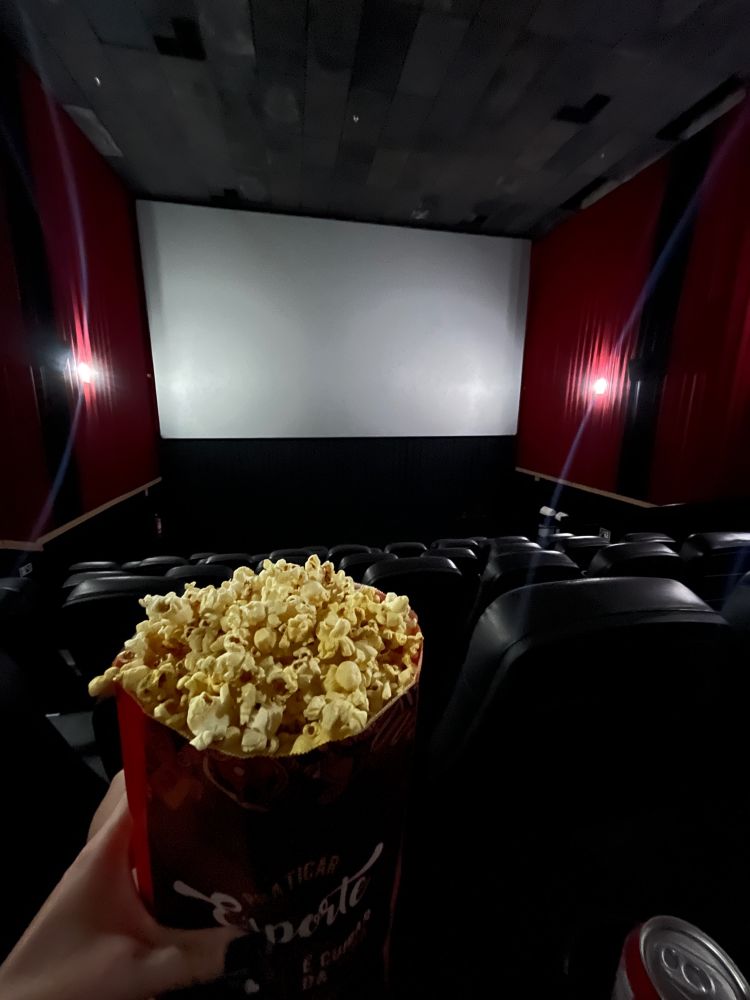 mão segurando um pacote de pipoca em uma sala de cinema vazia e com a tela desligada 