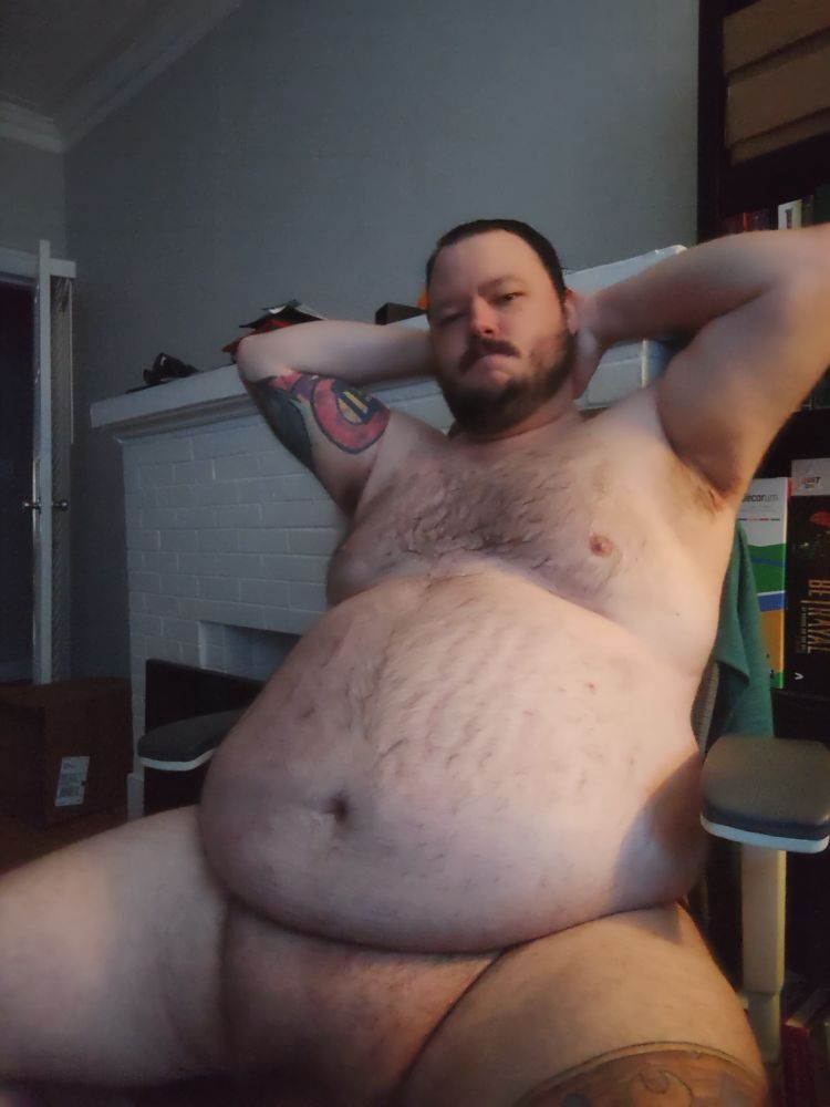 Photo of a nude chubby man with his arms behind his head