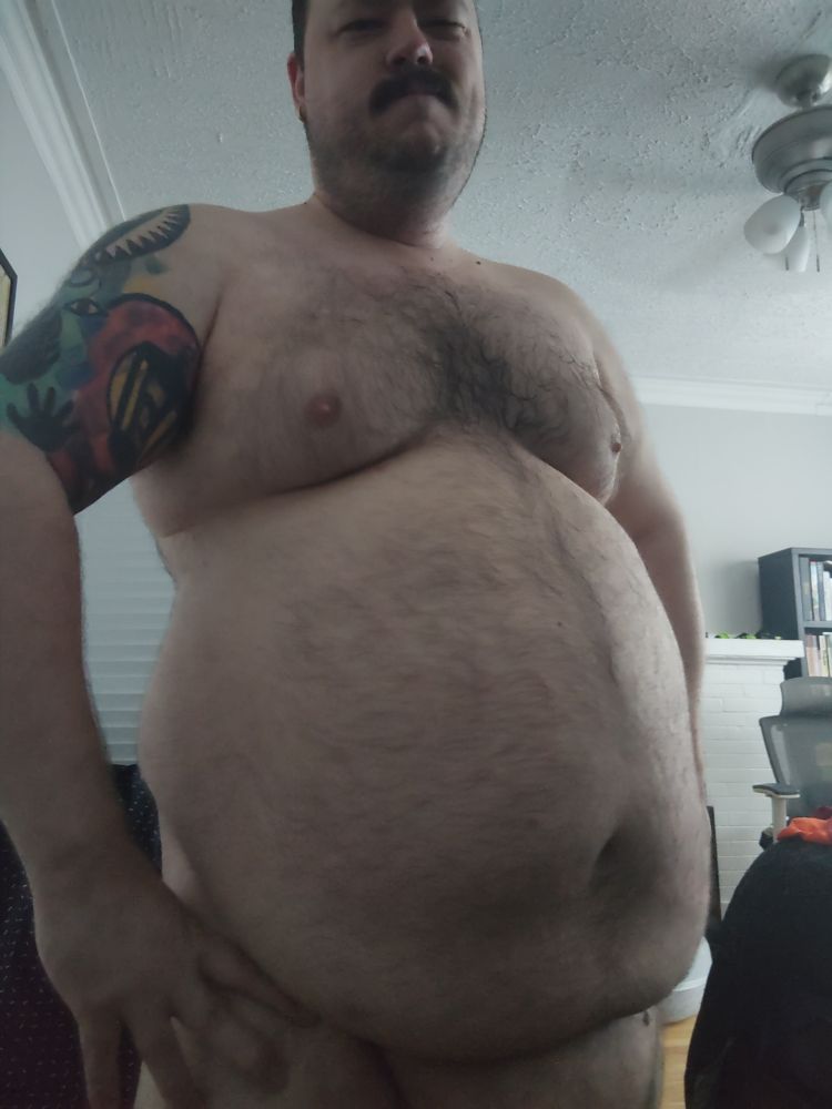 A chubby man facing the camera, nude, but the photo ends just below waist level