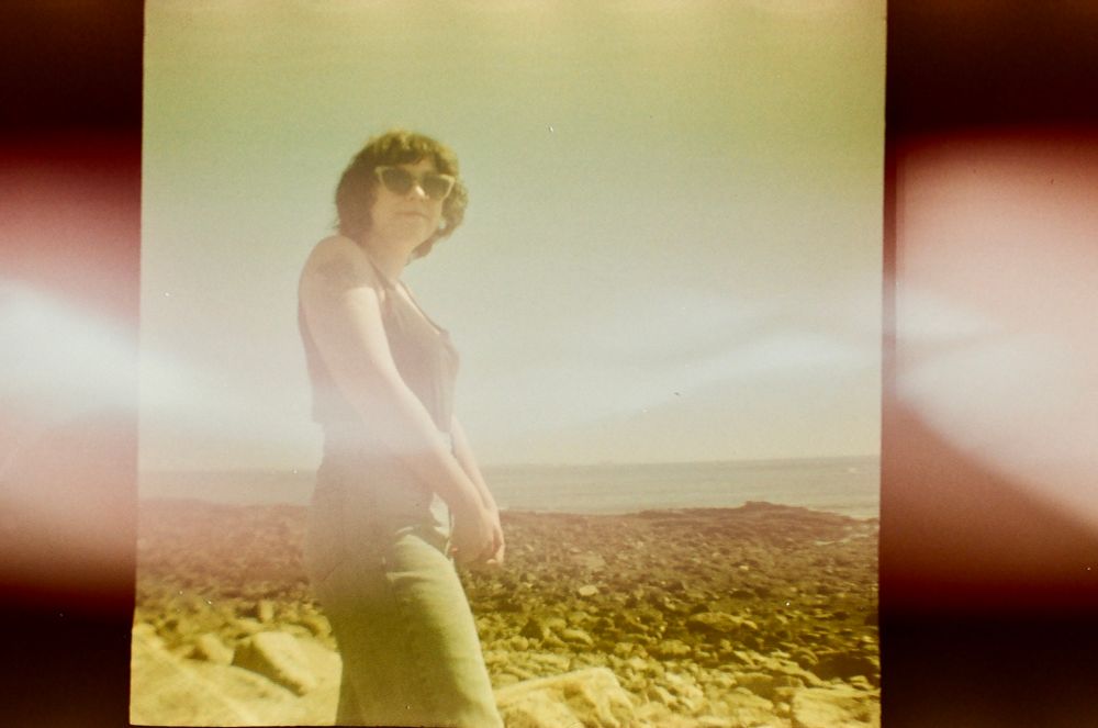 Old fujifilm photo taken by a Diana mini of a young woman at a beach 