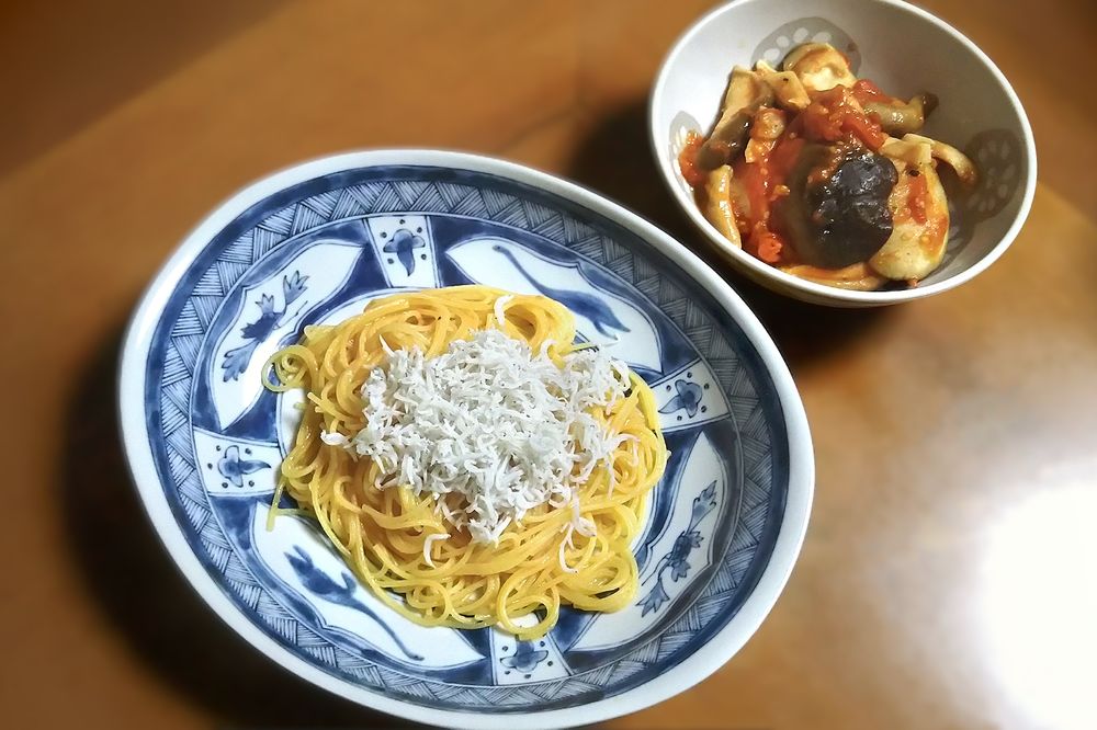 夕飯の写真。手前やや左、染付の楕円の深皿にパスタ。右奥、見込みに薄い灰色で蓮根の柄が入った浅めの白の丼に平茸。