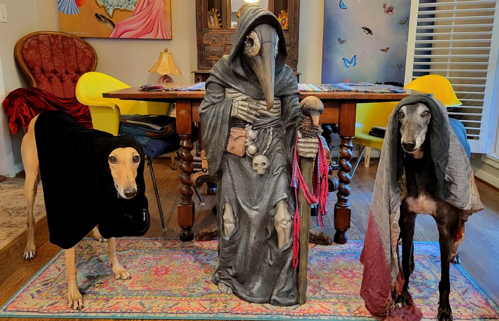 2 greyhounds and a statue of a plague doctor. 