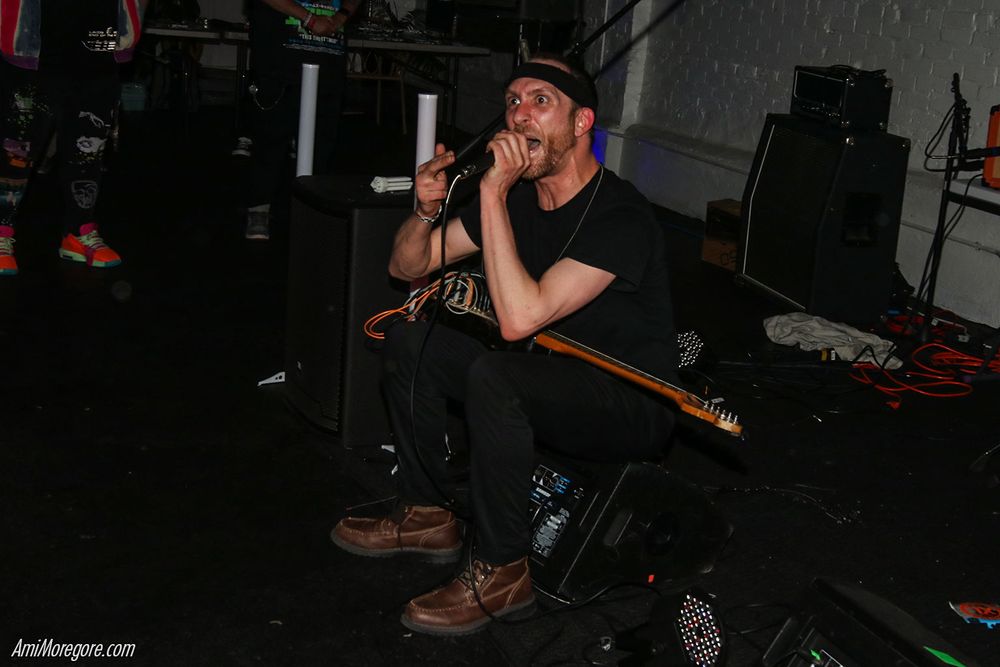 Kevin from Math the Band sits on a monitor with a guitar on his lap