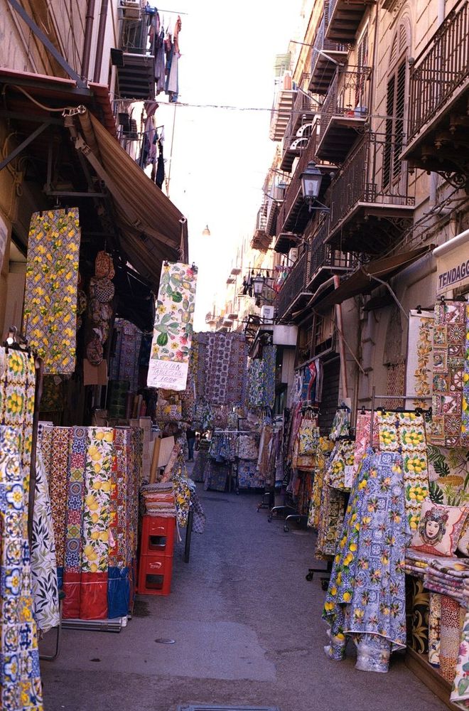 Eine Gasse, in der auf beiden Seiten verschiedenste bunte Stoffe hängen. 