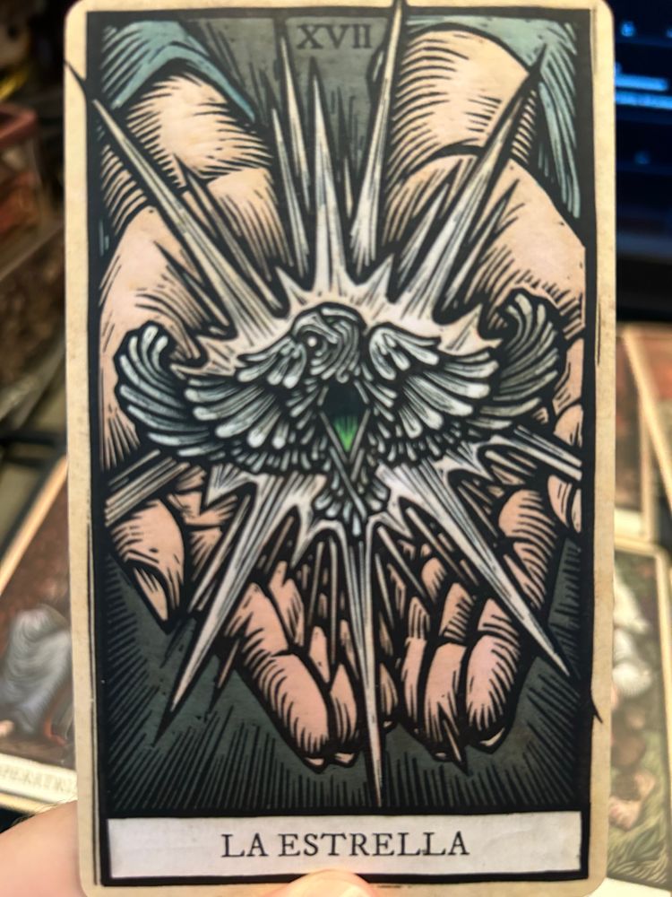 Carta de la estrella del tarot de El señor de los anillos de Tomás Hijo. Se trata del colgante de Arwen, en forma de pájaro y con una piedra verde en el centro, siendo sujetado por las manos de Arwen.