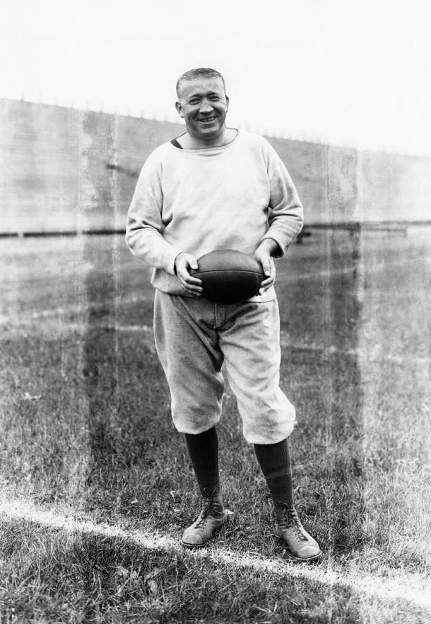 Notre Dame football coach Knute Rockne in a sweatshirt conducting a practice while holding a football