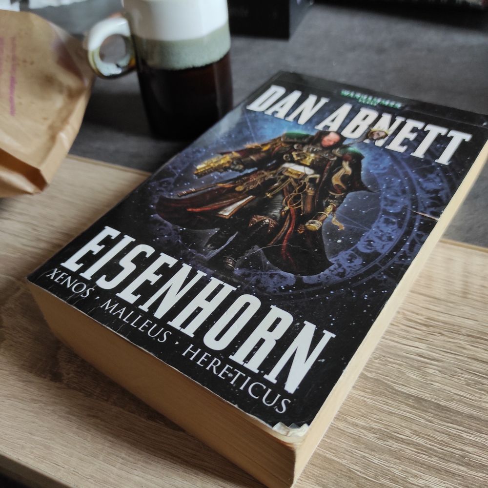 Gros plan d'un livre posé sur une table basse : l'omnibus Eisenhorn de Dan Abnett. Sur la couverture la silhouette sur fond noir d'un inquisiteur de W40k.