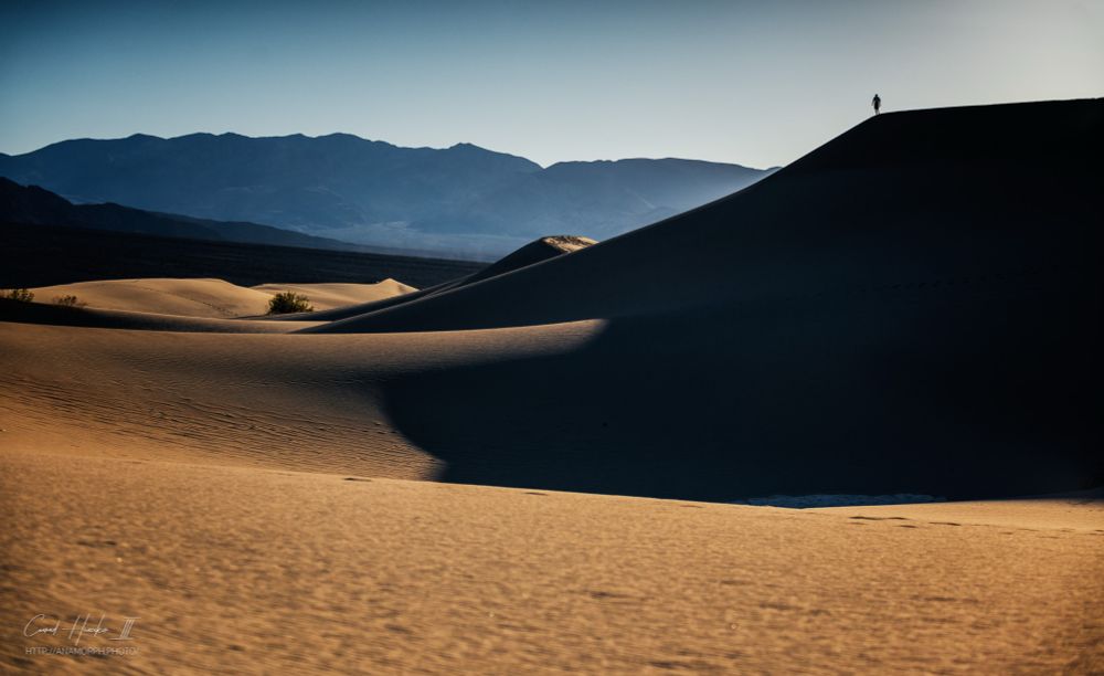 A person in the distance walks on the top of a towering dune in Death Valley 