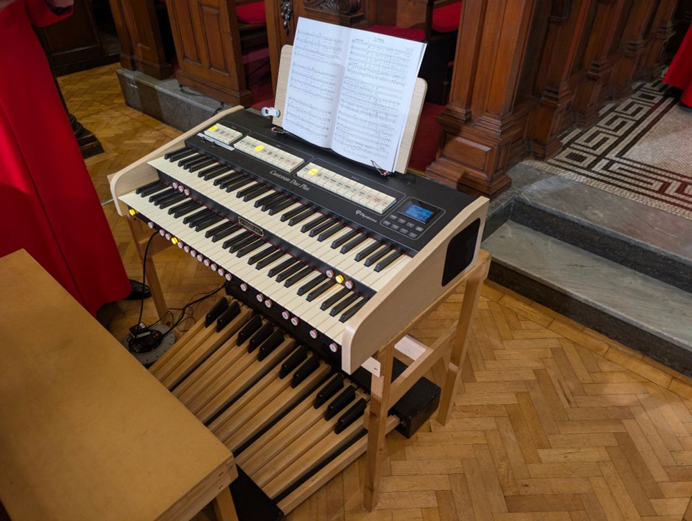 Organ console, with two hand keyboards, and one foot keyboard. On a wooden floor.