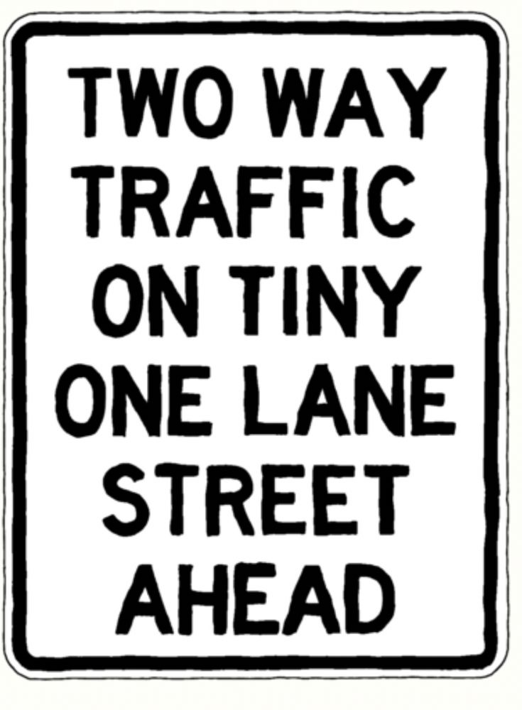 Satirical sign -rectangular white with black lettering with a thin black line bordering. It says in all caps:
TWO WAY 
TRAFFIC
ON TINY 
ONE LANE 
STREET
AHEAD



