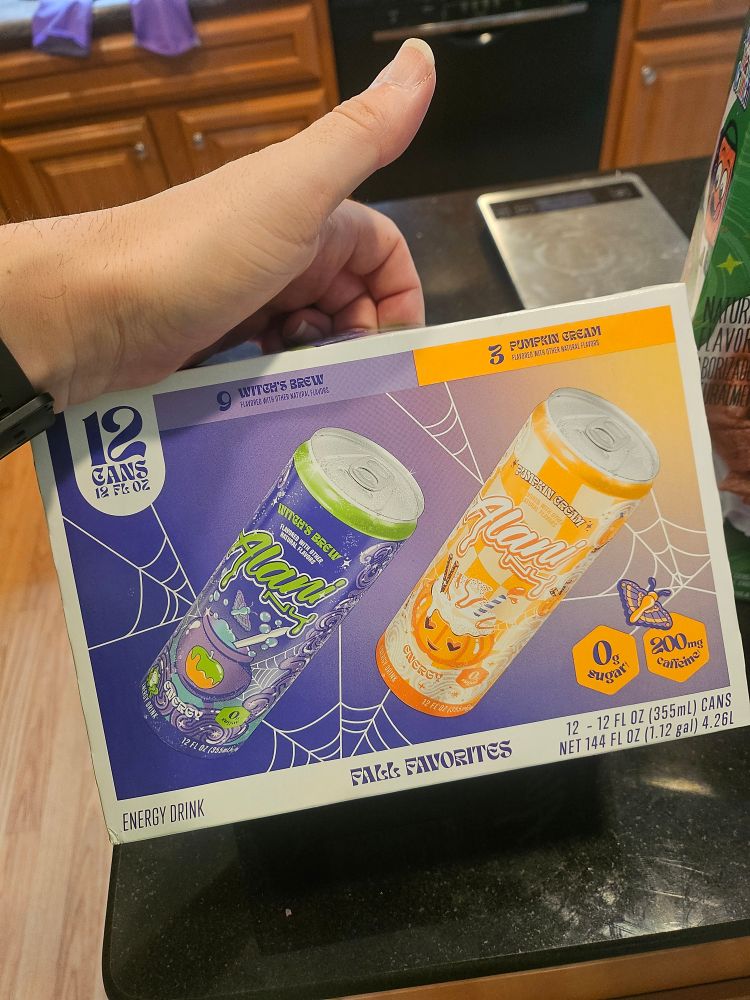 A case of Alani Nu energy drinks with two flavors - Witch's Brew (caramel apple) and Pumpkin Cream (pumpkin spice) the box is purple and orange with cobwebs
