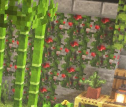 A Minecraft screenshot, showing vines growing over a wall of redstone ore blocks, making them look like the vines have red flowers