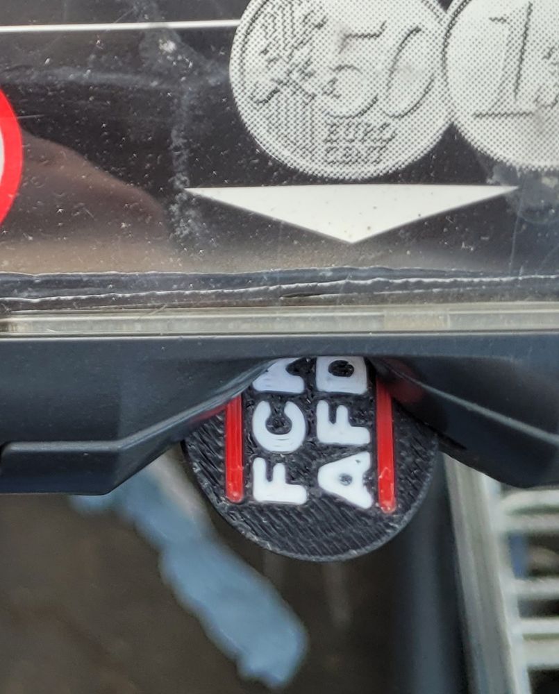 Bildausschnitt mit einem FCK AFD Einkaufswagenchip im Schlitz vom Griff eines Einkaufswagens.