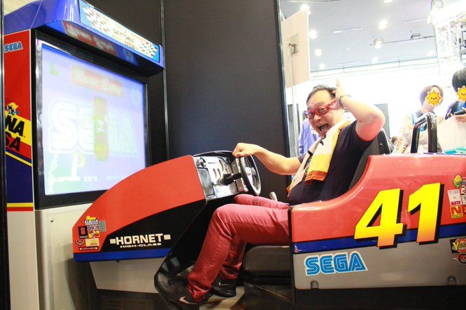 Takenobu Mitsuyoshi, the composer for Sega's Daytona USA is playing the Araacde game and smiling