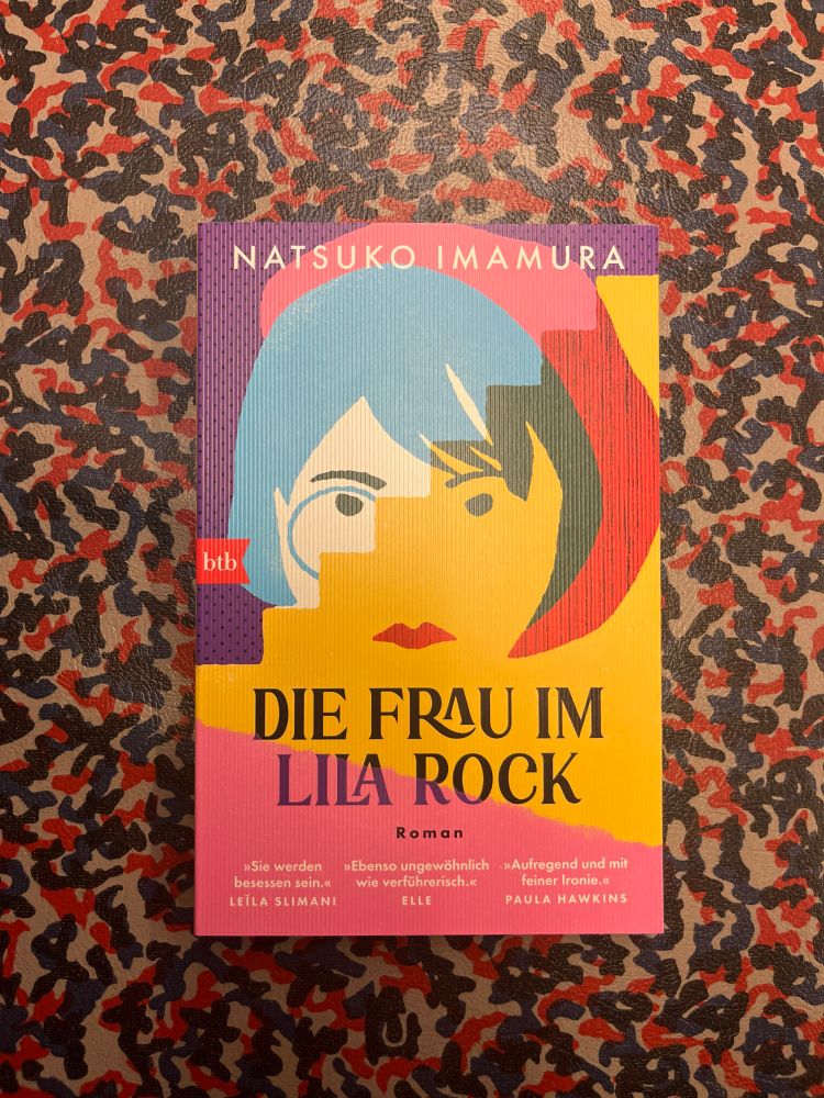 Taschenbuch „Die Frau im Lila Rock“ von Natsuko Imamura. Das Buch liegt auf dem gefleckten Muster der BVG U-Bahn in Berlin. 