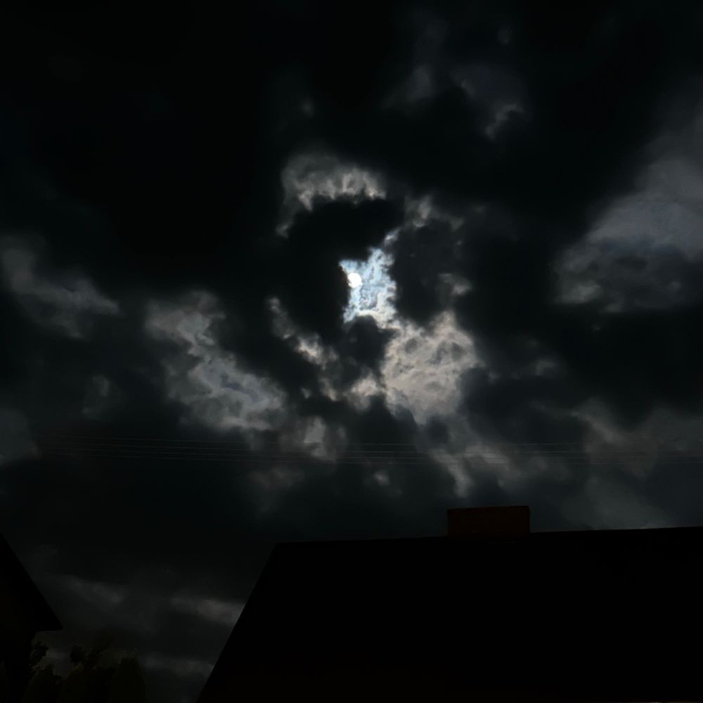 Pic of night sky - very cloudy, dark and heavy clouds. Quality of the tiny piece of moon is crap but the lighting looks as if somebody was using a super-ultra-god-like torch/flashlight from behind the clouds (harsh, flash-like white light).