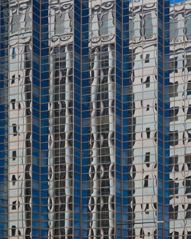 A picture of a glass building reflecting a building with columns