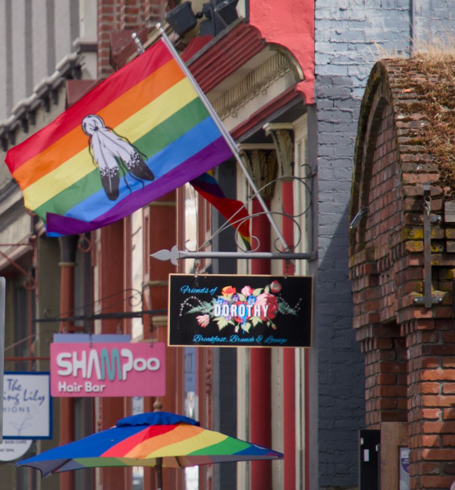 A picture of the Friends of Dorothy Breakfast, Brunch, and Lounge sign in Victoria, BC with a two spirit pride flag above it and a rainbow umbrella below it.