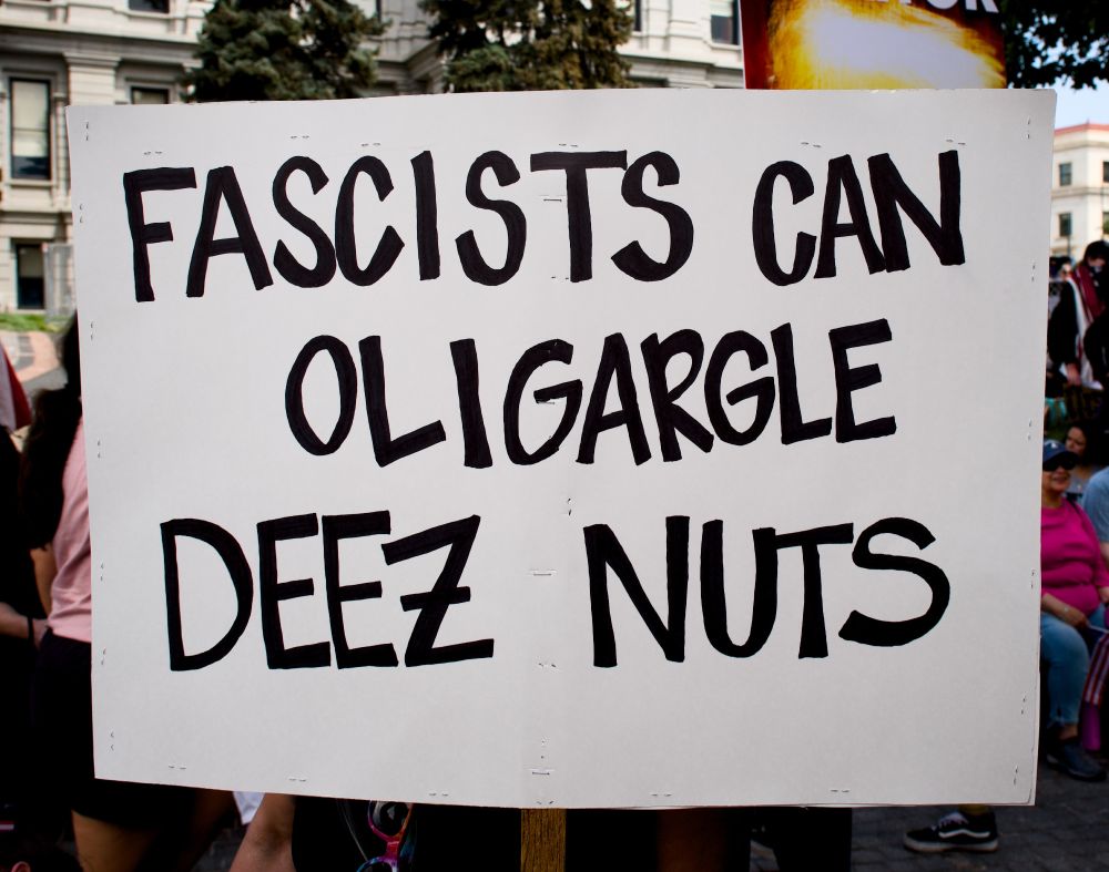 A photo of a sign saying "FASCISTS CAN OLIGARGLE DEEZ NUTS"