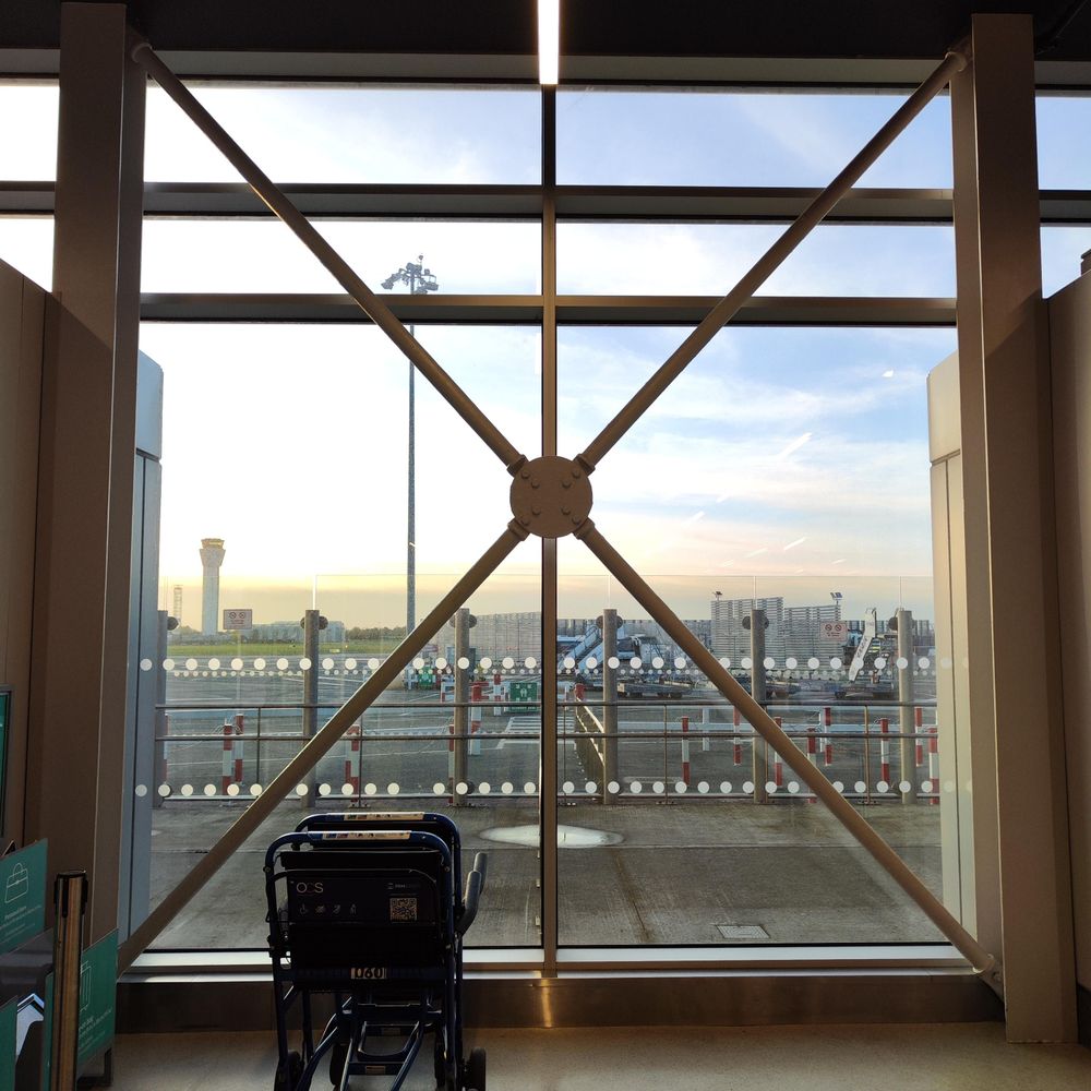 Large window at an airport, with some wheelchairs in front of it, reinforced by six strong radial bars interesting at the centre