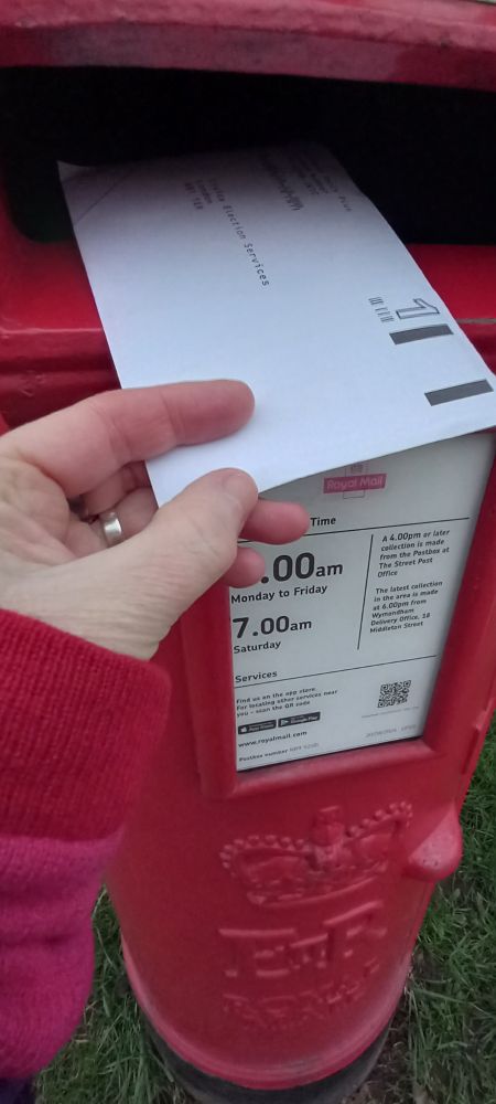 Photo of a ballot envelope being posted into a post box.