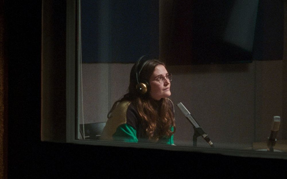 Una mujer dentro de un estudio de radio, lleva auriculares y tiene un micrófono delante. Fotograma de 'La nostra habitació'.