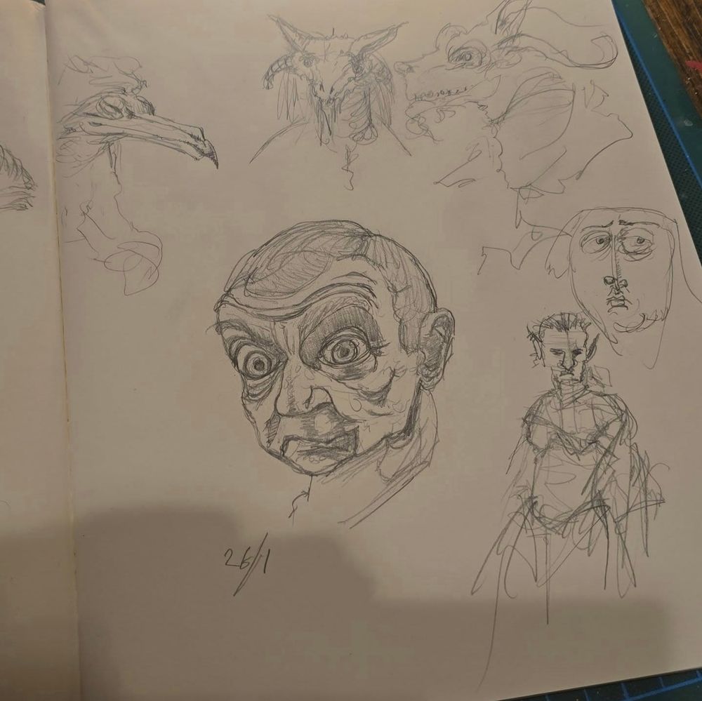 Photo of a sketchbook page with quick pencil sketches of human and monster faces